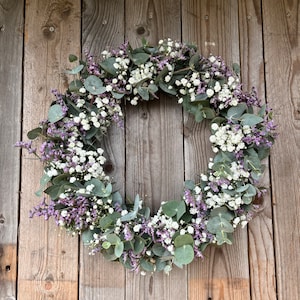 May include: A wreath made of eucalyptus leaves and white baby's breath flowers with purple accents.