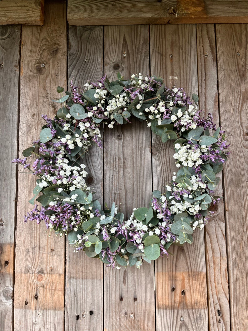 May include: A wreath made of eucalyptus leaves and white baby's breath flowers with purple accents.