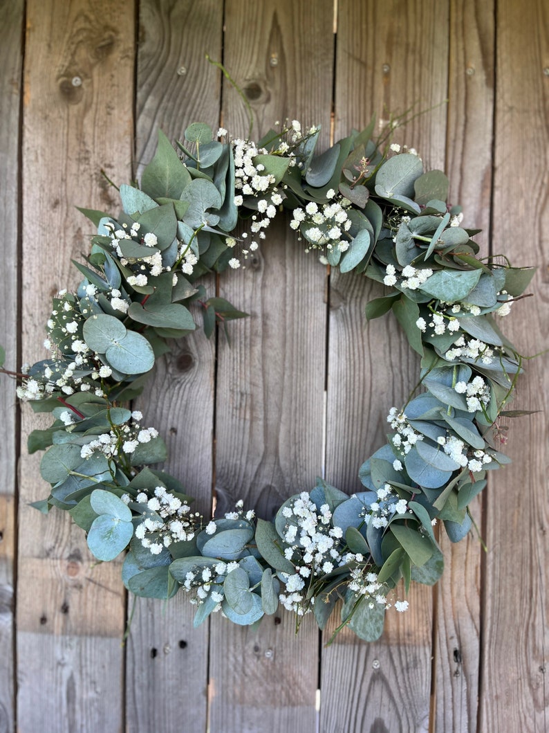 May include: A green eucalyptus and white baby's breath wreath hanging on a wooden fence.