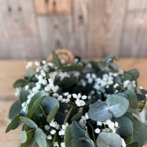 May include: A green eucalyptus wreath with white baby's breath flowers.