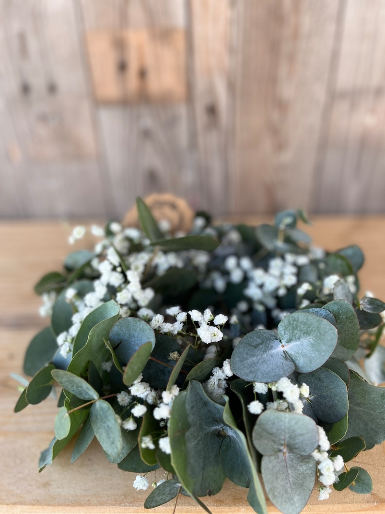 May include: A green eucalyptus wreath with white baby's breath flowers.