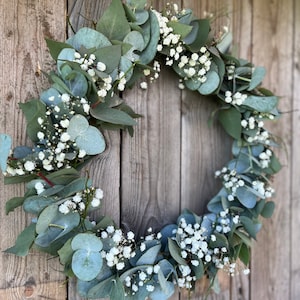 May include: A green and white eucalyptus and baby's breath wreath hanging on a wooden door.