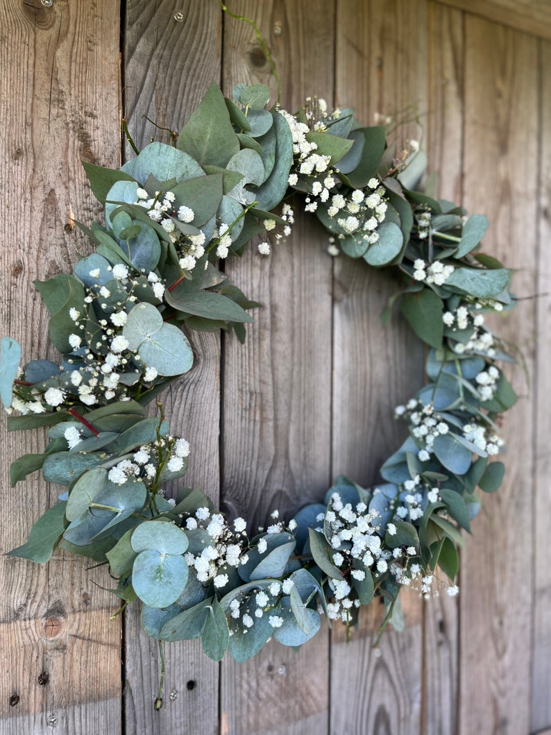 May include: A green and white eucalyptus and baby's breath wreath hanging on a wooden door.