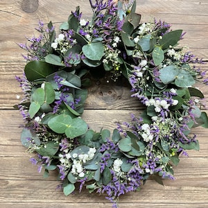 May include: A wreath made of eucalyptus leaves and small purple and white flowers.