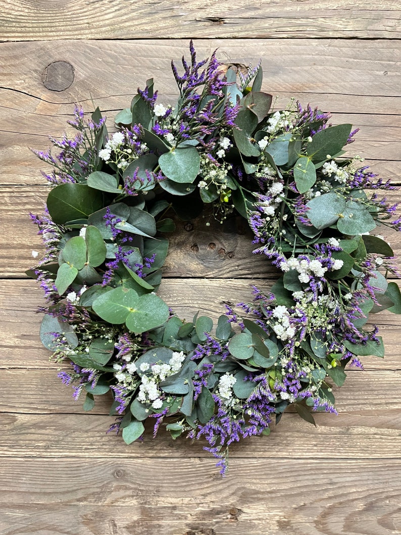 May include: A wreath made of eucalyptus leaves and small purple and white flowers.
