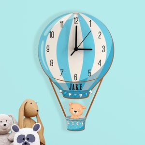 May include: A blue and white hot air balloon clock with the name "JAKE" printed on the bottom. A brown teddy bear is sitting in the basket of the balloon.