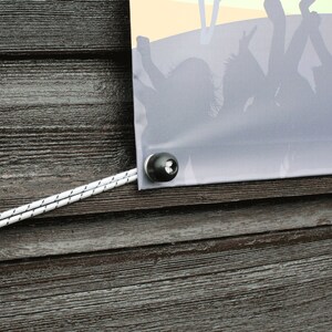 May include: A banner with a crowd silhouette, secured with a black grommet and white rope against a weathered wood background. The banner has a gradient of colors, with a yellow and orange sky.