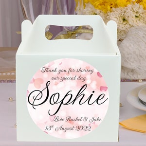 May include: White favour box with a pink and white circular sticker. The sticker has the text "Thank you for sharing our special day Sophie Love Rachel & Jake 13th August 2022".