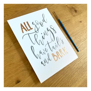 May include: A white card with the phrase "ALL good things have tails and BARK" written in black and copper calligraphy.