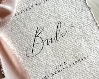 Può includere: Un biglietto bianco con una superficie testurizzata e il testo "Letters to the Bride" scritto in nero. La parola "Bride" è scritta in corsivo. Sotto il testo c'è il nome "Saima Remina Farhana" e la parola "Love".