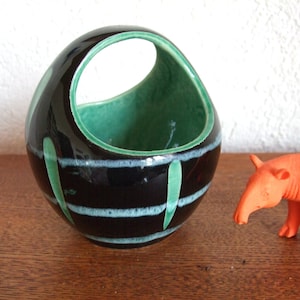 Könnte beinhalten: Ein schwarzer Keramiktopf mit grünem Innenraum und einem Henkel. Der Topf hat ein gestreiftes Design mit weißen und grünen Akzenten.