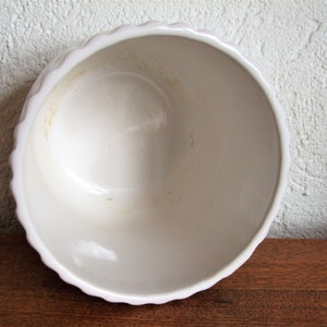 K&ouml;nnte beinhalten: Wei&szlig;e Keramiksch&uuml;ssel mit gewelltem Rand. Die Sch&uuml;ssel hat eine leicht gebrochenwei&szlig;e Farbe und weist Gebrauchsspuren mit einigen hellbraunen Flecken auf.