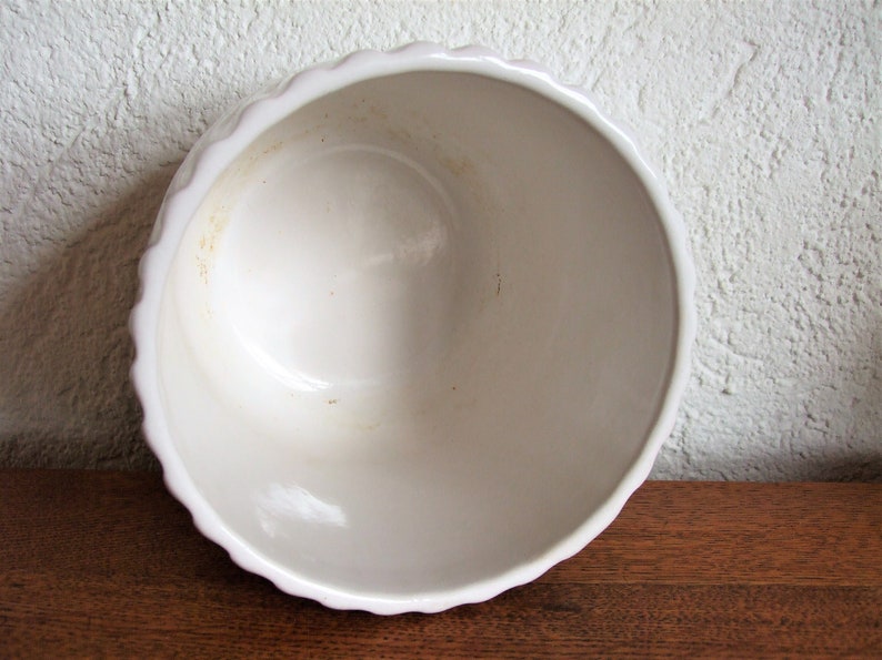 K&ouml;nnte beinhalten: Wei&szlig;e Keramiksch&uuml;ssel mit gewelltem Rand. Die Sch&uuml;ssel hat eine leicht gebrochenwei&szlig;e Farbe und weist Gebrauchsspuren mit einigen hellbraunen Flecken auf.