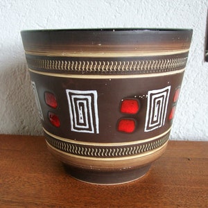 Könnte beinhalten: Ein brauner Keramiktopf mit einem geometrischen Muster in Weiß und Rot. Der Topf hat einen breiten Rand und einen abgerundeten Boden.