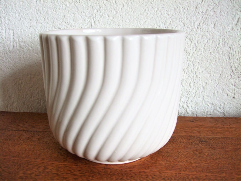 K&ouml;nnte beinhalten: Wei&szlig;er Keramiktopf mit wellenf&ouml;rmigem, geripptem Design. Der Topf ist leer und steht auf einer Holzoberfl&auml;che.