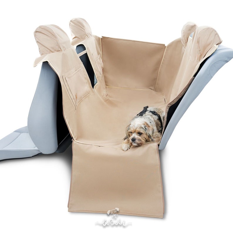 May include: Beige car seat cover with a small dog lying on it. The cover has two headrest covers and a flap that covers the back of the seat. The cover is made of a water-resistant material.