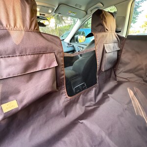 May include: Brown car seat cover with a mesh divider and pockets. The cover is made of a water-resistant material and has a logo on the bottom left corner.