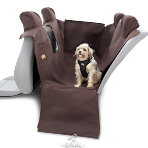 May include: Brown car seat protector with a small dog sitting on it. The protector has two headrest covers and a pocket on the back. The dog is wearing a black harness.