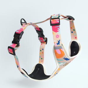 May include: A pink, blue and yellow patterned dog harness with a black adjustable buckle. The harness has a padded chest piece for comfort.