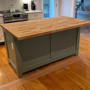 May include: A kitchen island with a light green base and a wood countertop. The island is in a room with hardwood floors.