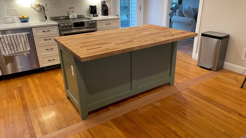 May include: A kitchen island with a light green base and a wood countertop. The island is in a room with hardwood floors.