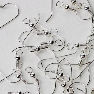 May include: A close-up of a pile of silver earring hooks. The hooks are made of metal and have a small ball at the top. They are designed for making earrings.