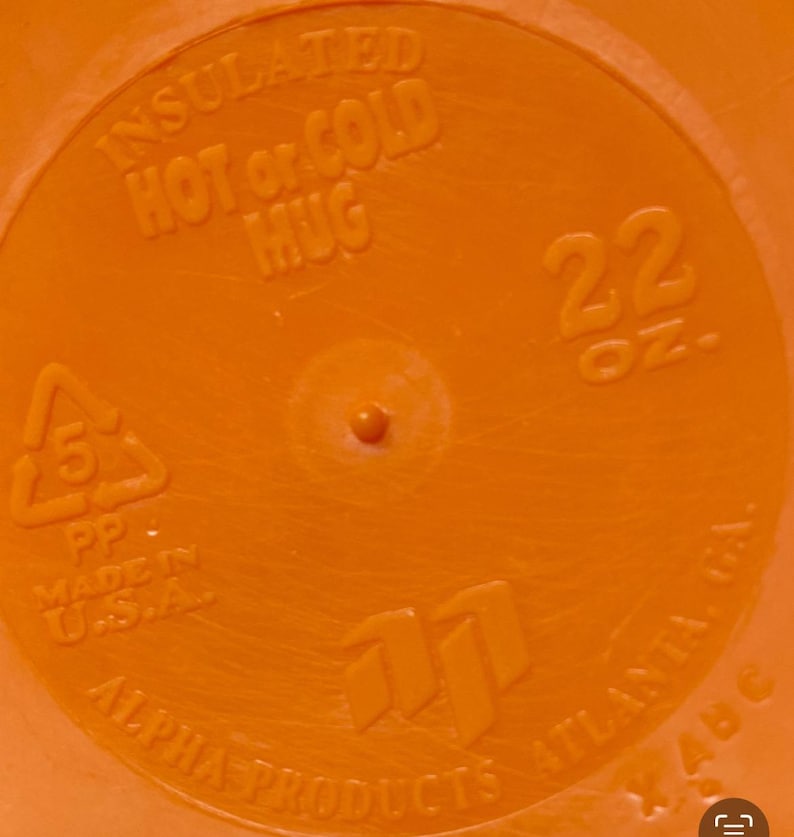 Peut inclure: Gros plan sur un mug isotherme orange. Le mug porte l'inscription "INSULATED HOT or COLD MUG" et "22 OZ.". Le bas du mug indique "ALPHA PRODUCTS ATLANTA, GA." et "MADE IN U.S.A."