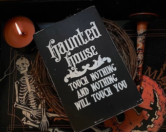 Puede incluir: Un letrero de madera negro con texto blanco que dice "Haunted House Touch Nothing And Nothing Will Touch You". El letrero está rodeado de una corona de ramas marrones y una decoración de esqueleto.