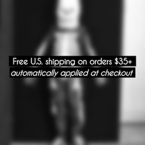 Peut inclure: Image en noir et blanc avec le texte "Free U.S. shipping on orders $35+ automatically applied at checkout". Une silhouette floue est au centre, sur fond sombre.