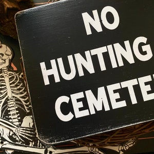 Op de afbeelding: Zwart houten bord met witte tekst die "NO HUNTING CEMETERY" luidt.
