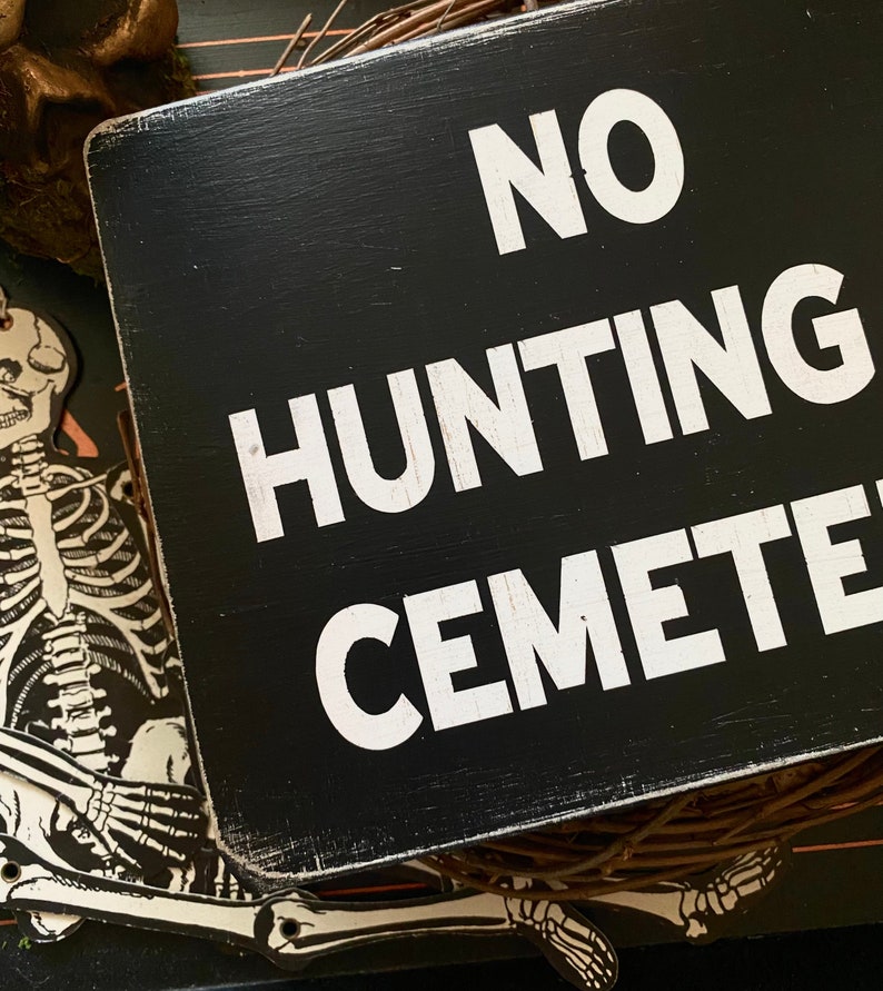 Op de afbeelding: Zwart houten bord met witte tekst die "NO HUNTING CEMETERY" luidt.