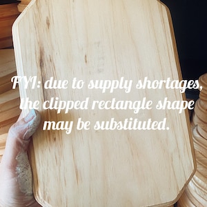 May include: A light-colored, rectangular wooden plaque with clipped corners is held in a hand. The text "FYI: due to supply shortages, the clipped rectangle shape may be substituted" is visible on the plaque.