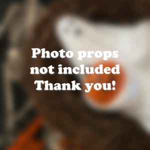 Op de afbeelding: Wazige afbeelding met de tekst "Photo props not included Thank you!" in het wit. De afbeelding toont een mannequinhoofd en een wazig oranje object op de achtergrond.