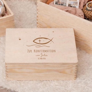 Könnte beinhalten: Eine hellfarbene Holzkiste mit Deckel, mit einem Fischsymbol und dem Text "ZUR KONFIRMATION von Julia 02. Mai 2026". Die Kiste ist rechteckig und scheint Teil eines Sets zu sein, mit anderen Holzkisten im Hintergrund.