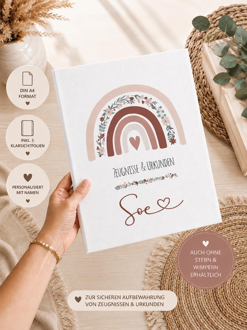 May include: A white binder for certificates and documents featuring a boho-style rainbow illustration with floral accents in muted earth tones. The text reads "ZEUGNISSE & URKUNDEN" and the name "Soe" with a heart symbol below the rainbow.