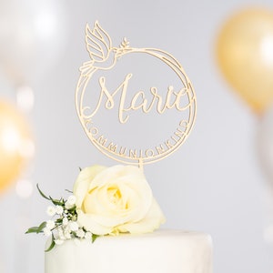Può includere: Un topper per torta in legno dorato con una colomba e il nome "Marie" in un cerchio con il testo "Communion Kind".