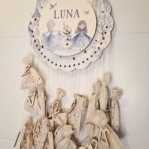Könnte beinhalten: Adventskalender aus Holz mit rundem Oberteil mit Illustrationen von Zeichentrickfiguren und dem Namen "LUNA". Der Kalender enthält kleine Stoffbeutel mit Holzzahlen, ideal zum Zählen bis zu einem besonderen Tag.