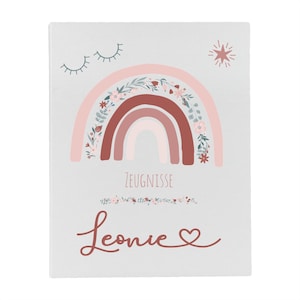 May include: A white rectangular folder featuring a printed design of a rainbow with floral accents, a star, and closed eyes. The text ZEUGNISSE is printed in the center, with the name Leonie and a heart symbol written in cursive below it.