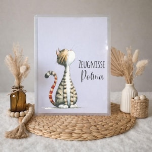 Peut inclure: Un classeur transparent avec une illustration de chat de dessin animé et le texte "ZEUGNISSE Polina". Le chat a une queue et un corps rayés. Le classeur est posé sur un tapis tressé.