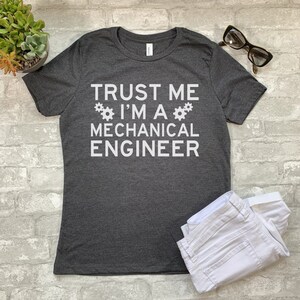 May include: Dark gray t-shirt with white text that reads "Trust me I'm a Mechanical Engineer" with two white gear symbols on either side of the text.