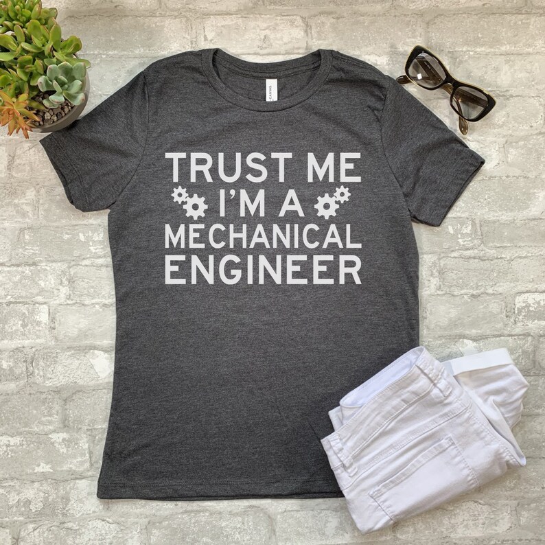 May include: Dark gray t-shirt with white text that reads "Trust me I'm a Mechanical Engineer" with two white gear symbols on either side of the text.