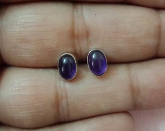 May include: A pair of silver stud earrings with oval-shaped purple gemstones.
