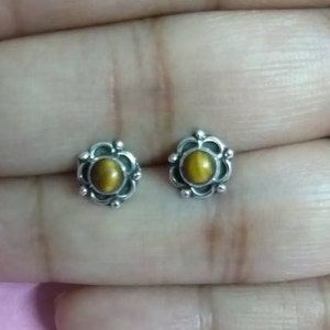 May include: A pair of silver earrings with a brown tiger's eye gemstone in each. The earrings have a floral design.
