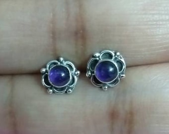 May include: A pair of silver stud earrings with a purple amethyst gemstone in each. The earrings have a floral design.