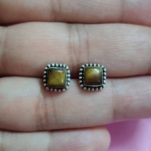 May include: A pair of silver stud earrings with square tiger's eye gemstones.