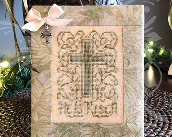 Peut inclure: Une broderie au point de croix encadrée dans un tissu vert et blanc avec les mots "Il est ressuscité" brodés en fil vert.
