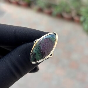 May include: A silver ring featuring a marquise-cut gemstone with a mix of deep green and burgundy hues. The stone is set in a polished silver band, creating a striking contrast. The ring's design is simple yet elegant, suitable for everyday wear or special occasions.