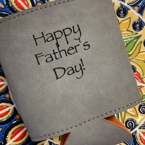 May include: Gray fabric can cooler with a stitched seam and a brown leather handle. The cooler has the text "Happy Father's Day!" printed on the front.