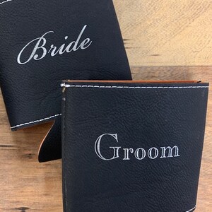 May include: Two black leather can coolers with white stitching. One cooler says "Bride" and the other says "Groom".