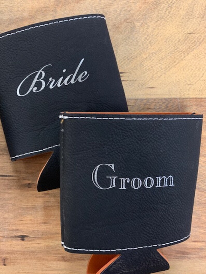 May include: Two black leather can coolers with white stitching. One cooler says "Bride" and the other says "Groom".